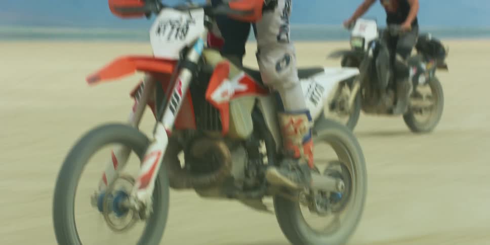 Man wearing a crash helmet rifes a motorcycle standing up through the desert