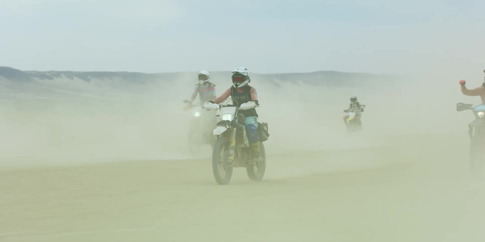 A group of friends riding through a dusty desert on dirt bikes