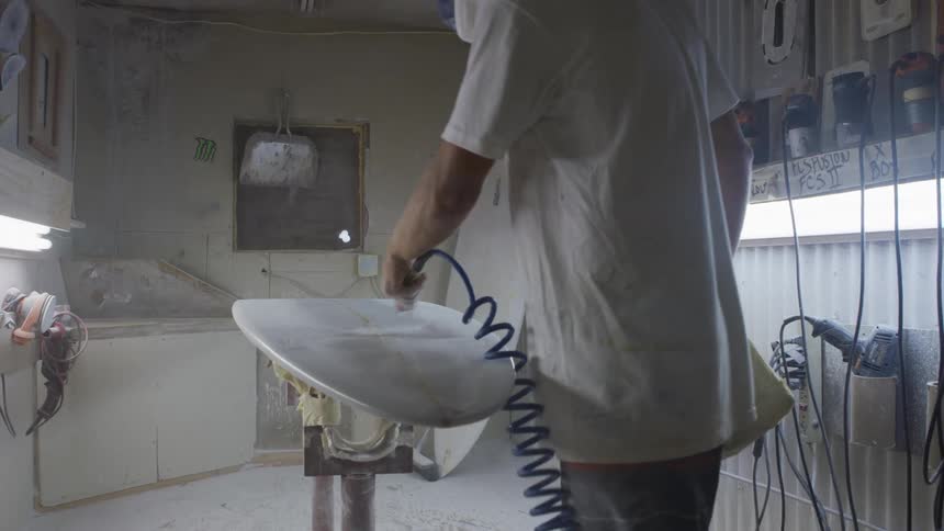 A man is using an air gun to dust off of a surfboard