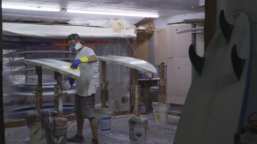 A man is pouring and smoothing wax on a surfboard
