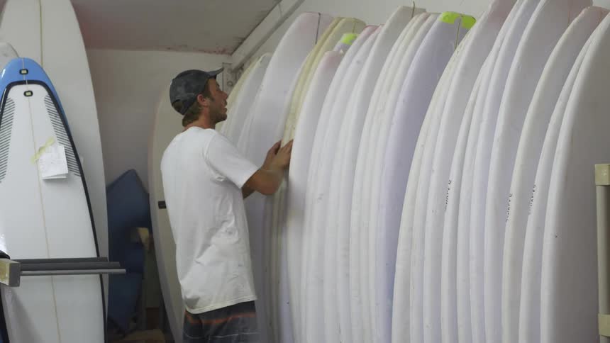 A man is looking through a row of unfinished surfboards