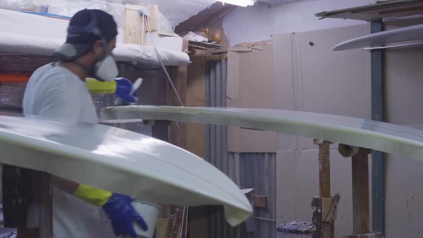 A male employee applying a coating to surfboards in a place of business