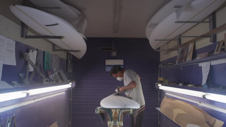 An employee working on a surfboard in a shop