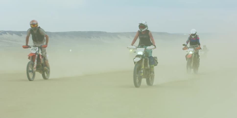 Group of people riding motorcycles on the desert kicking clouds of dust