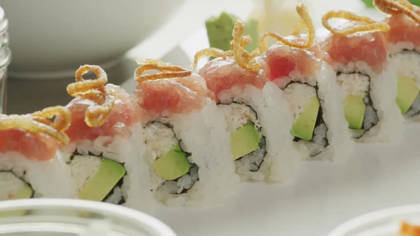 A sushi roll with fish and avocado sits on a white plate