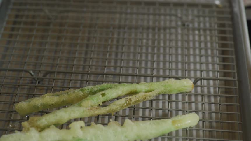 Person removes tempura vegetables from oil and places them on grill on tray to drain