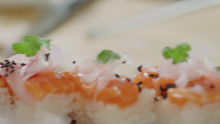 Cook sprinkles black sesame seeds over a plate of sushi