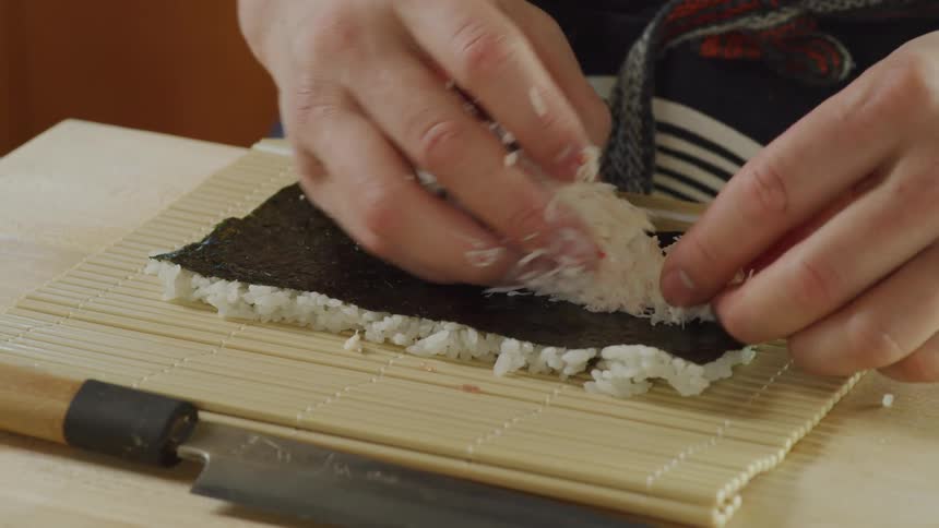 A chef preparing sushi on a bamboo mat in a restaurant