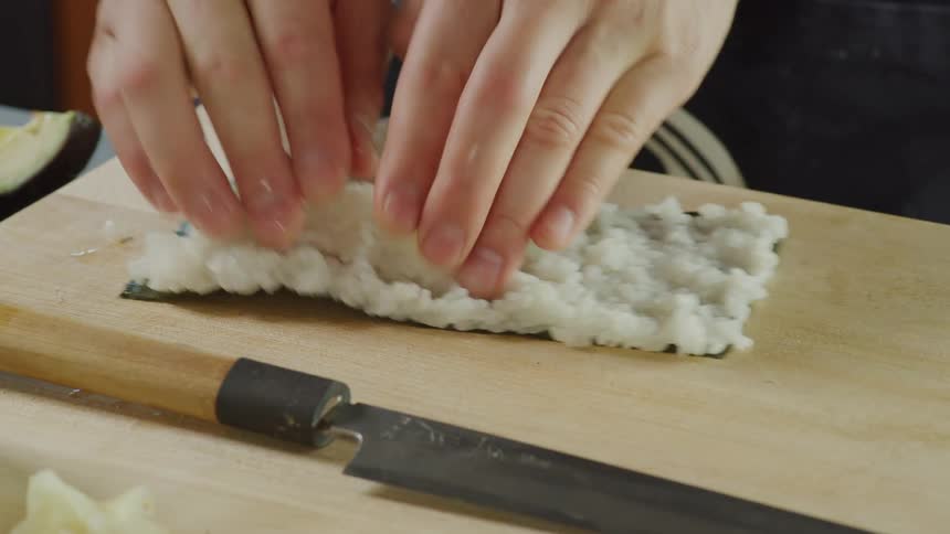 A person in a room preparing sushi on a cutting board with a knife