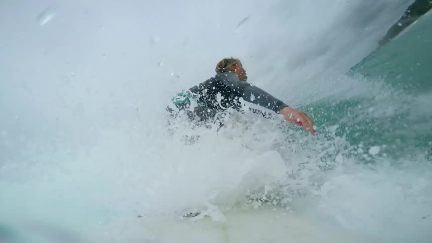 A boy swims atop his surfboard for a moment before rising to his feet and surfing until he falls off