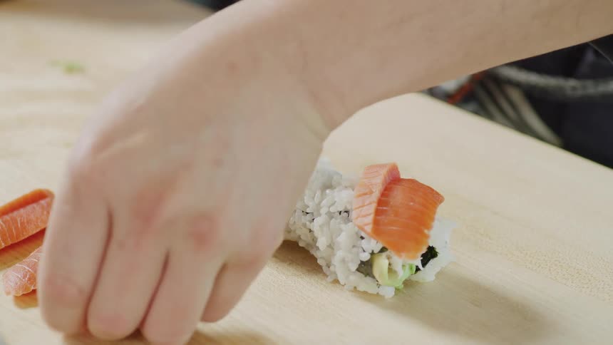 Person rolls sushi before topping it with small fish pieces