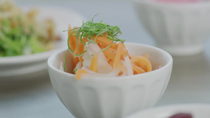 Vegetables and salads sit in bowls and plates on white surface
