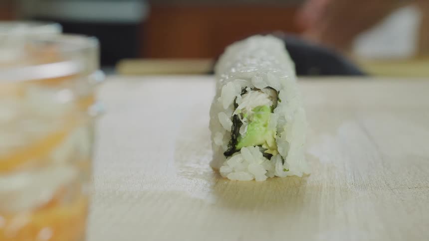 Sushi chef uses mat to shape sushi roll before topping it with protein