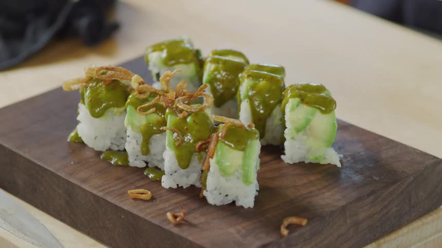 A person garnishing a sushi dish over a wooden board