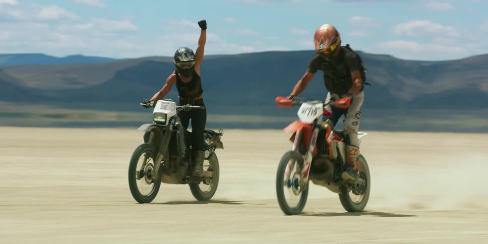 A man and woman riding dirt bikes out on a dry lakebed