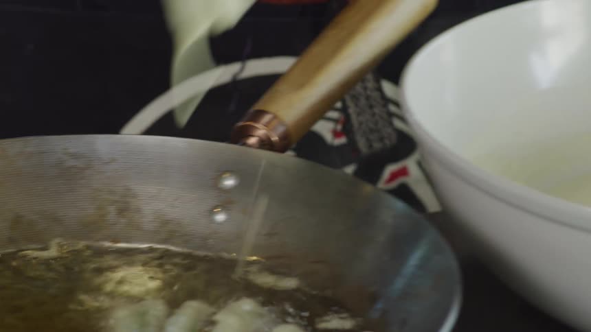 A person putting vegetables into a frying pan