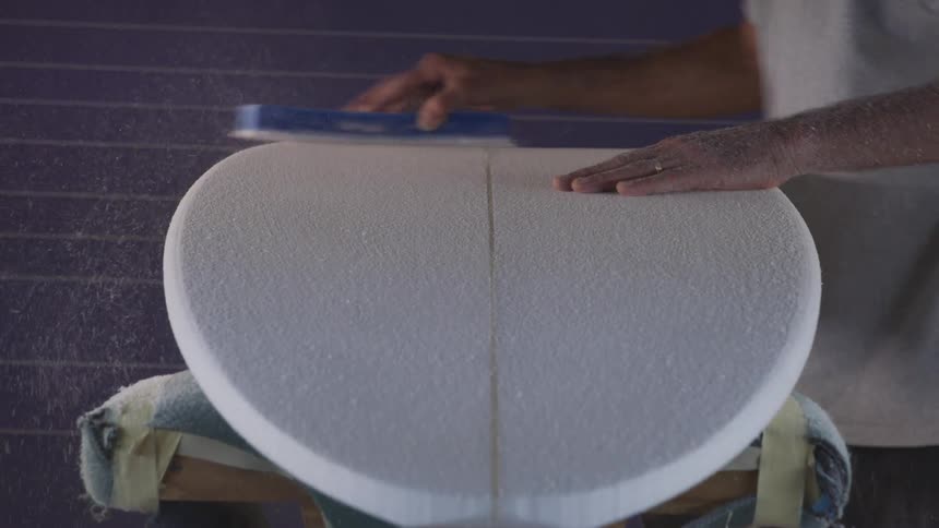 A man is sanding an unfinished surfboard