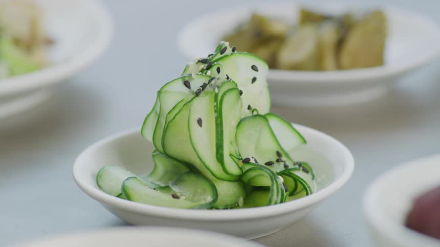 Plates of sliced cucumber and appetizers on a white table