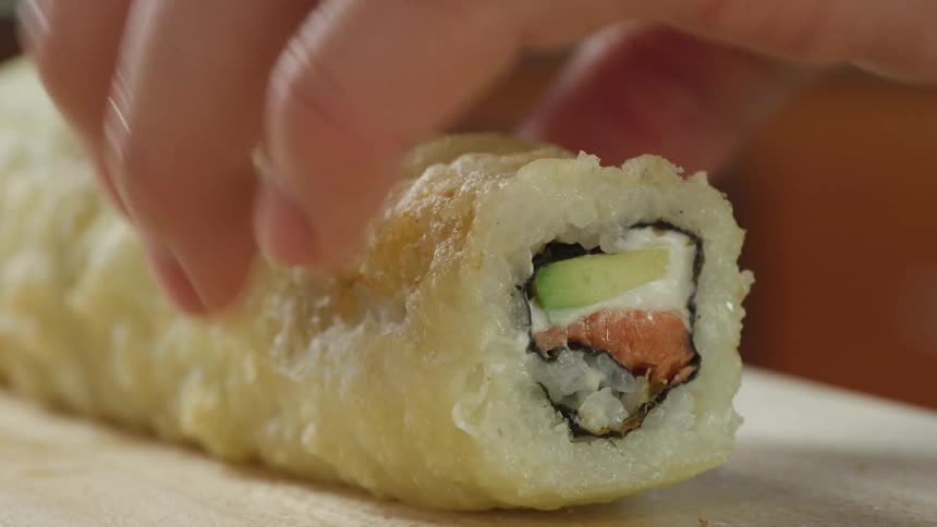 Chef slicing a roll of sushi with a sharp kitchen knife over a wooden board