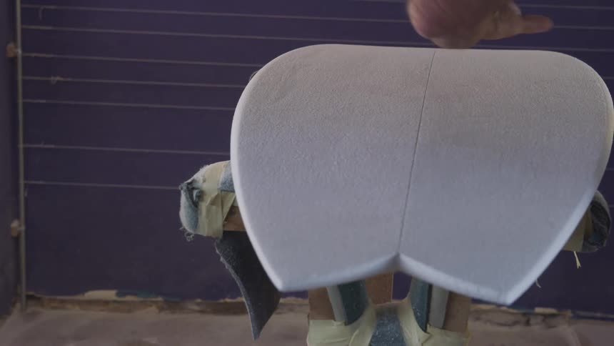 A man is polishing a surfboard in the shop
