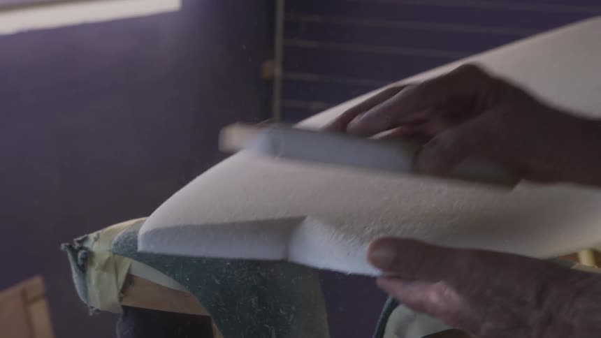 A person sanding a board with a sandpaper block indoors