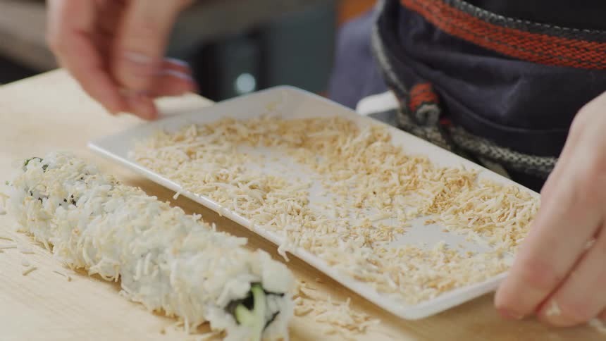 A person carefully prepares a sushi roll atop a wooden cutting board
