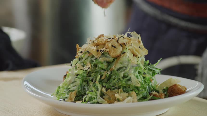 A chef adds garnish on top of a chopped salad on a plate