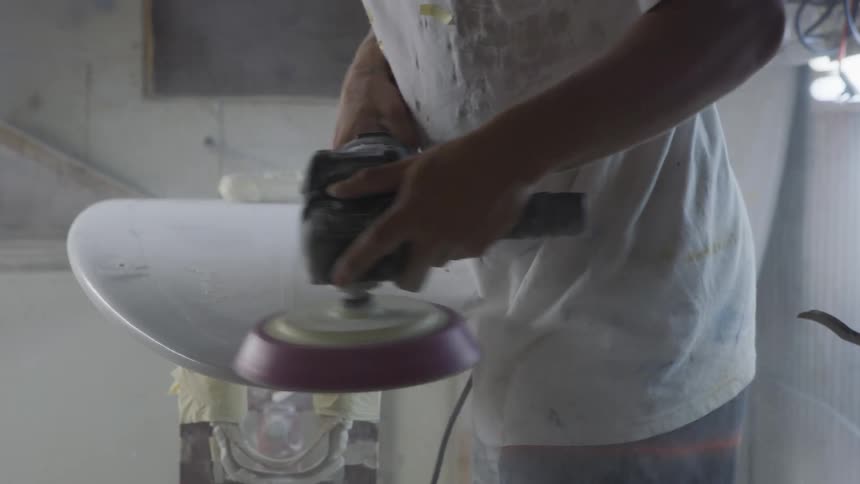 A man is buffing a surfboard with a tool