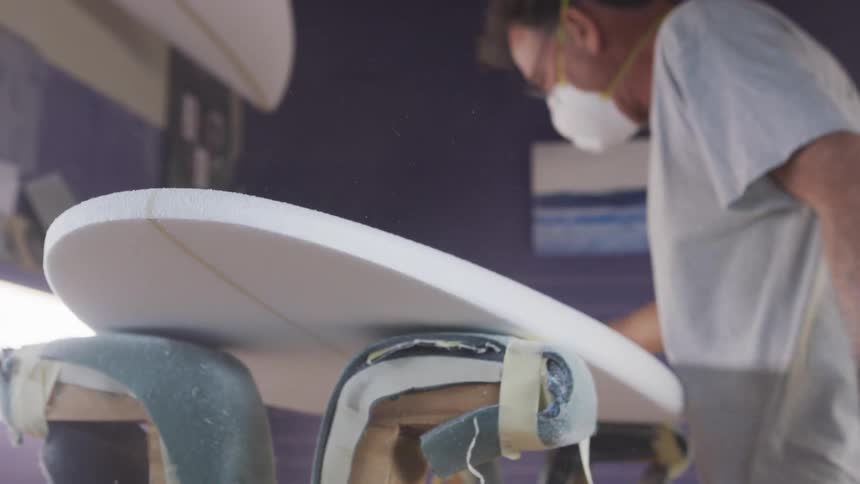 An employee sanding a surfboard in a shop