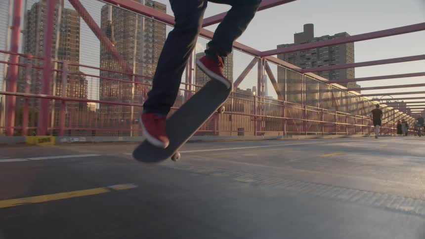 A man skateboards across a bridge with city buildings in the background