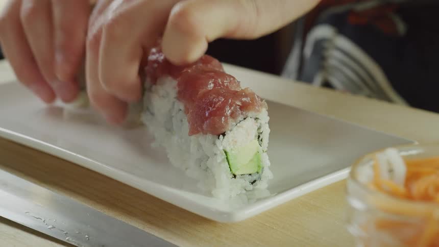 A person in a room placing sushi from a table onto a plate