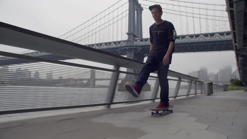 A young man riding a skateboard along the waterfront in an urban area