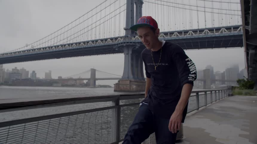 A skateboarder rides a skateboard on a boardwalk near an urban river with bridges