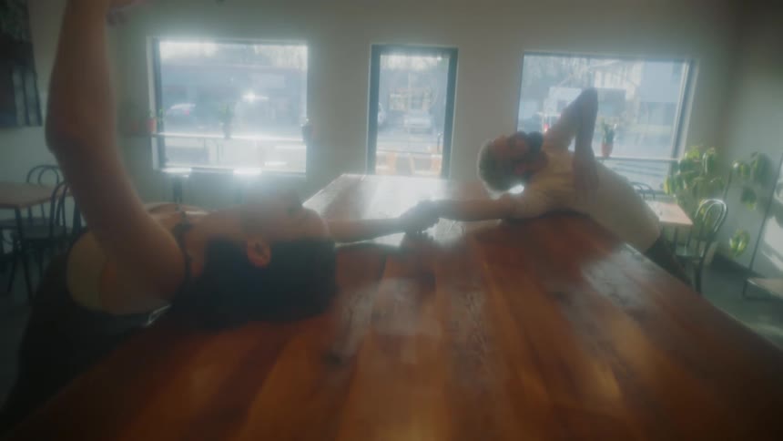 A man and a woman leaning on a table and dancing in a room with a wall and windows in the background