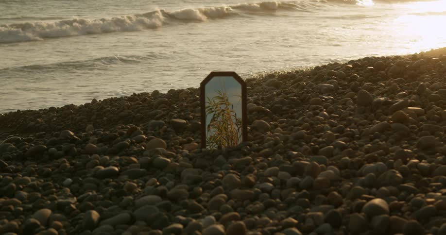 A small mirror stands upright in rocks along the sea shore