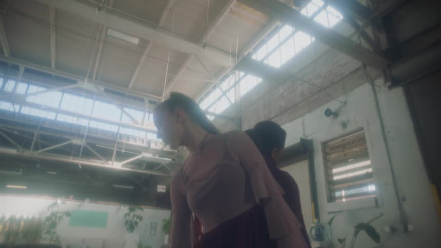 Two young women walk toward each other and stand back to back as they dance in a loft apartment