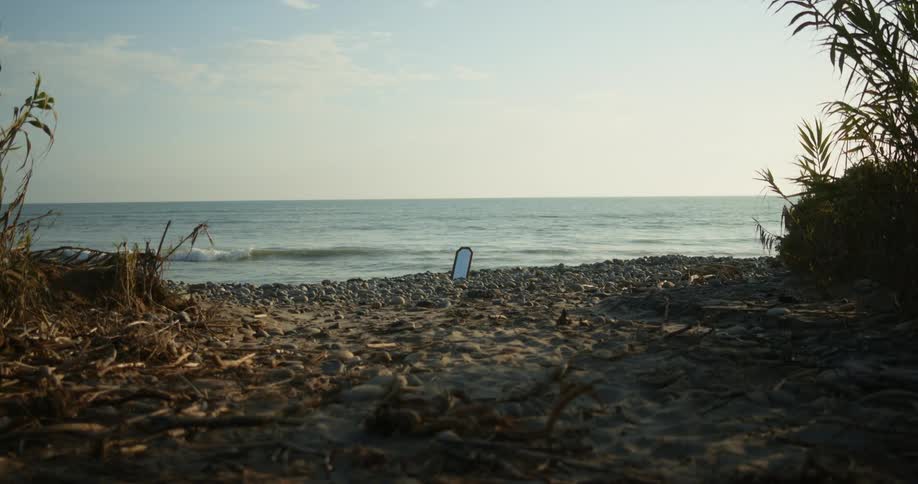 Mirror sits among pebbles on beach as waves roll onto shore