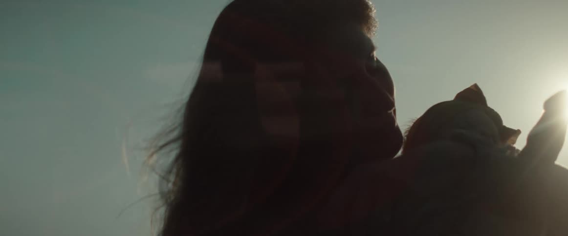 Woman partly silhouetted by sun shining from above holds baby girl