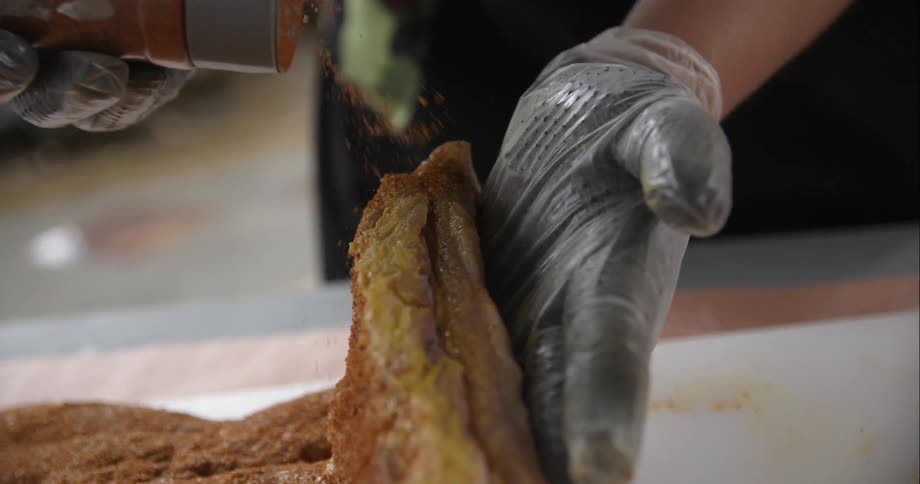 A man adds a generous amount of seasoning to a large piece of brisket