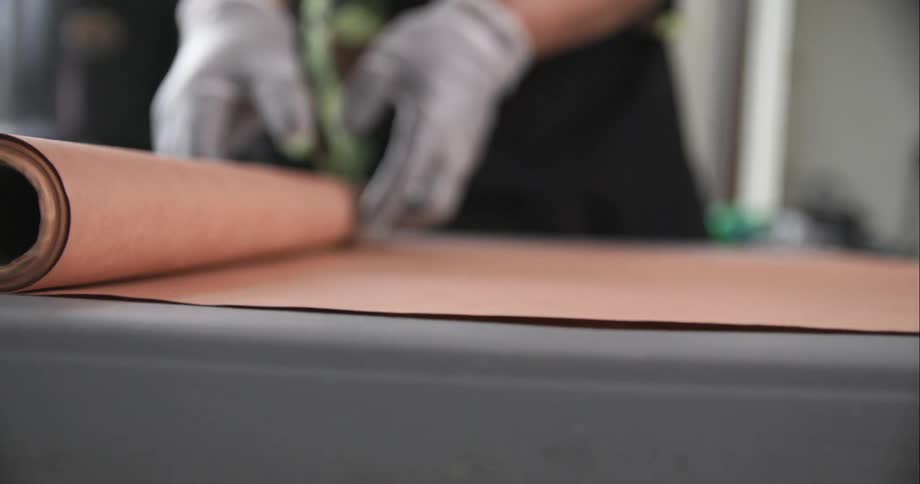 A gloved man rolls out several feet of butcher paper onto a long table