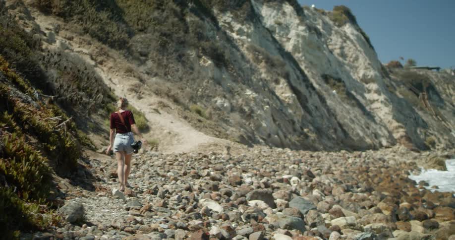 A woman walks along rocks on the coast