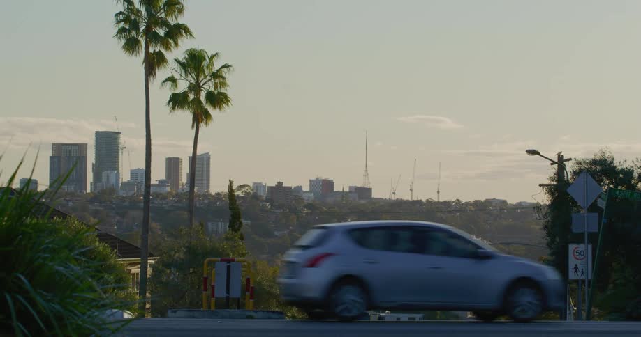 Early morning traffic passes by in a suburban area with a city skyline in the background