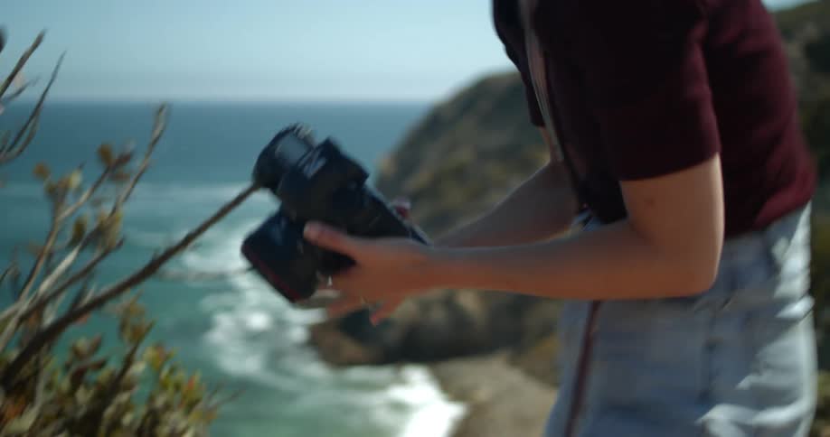 A woman lifts her camera from the bag by the cliff
