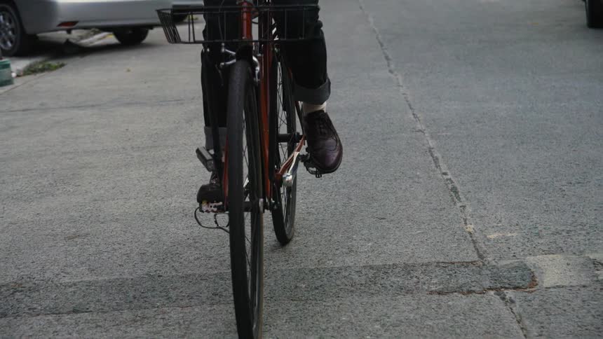 Person pedals bicycle along street past parked cars