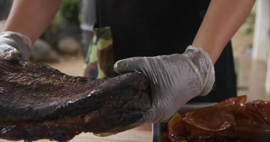 Chef removes a rack of seasoned marinated ribs from a pan over a wooden board