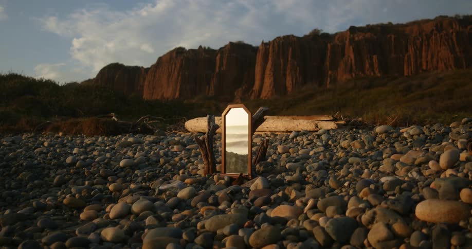 Ocean waves reflected on a mirror standing on the pebbles on a beach at sunset