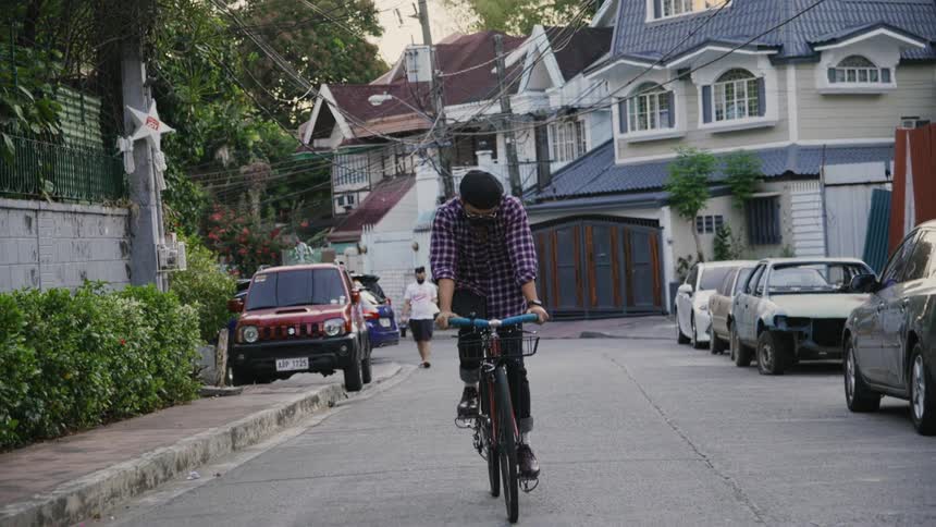 Man wearing face mask pedals along street with pedestrians in background