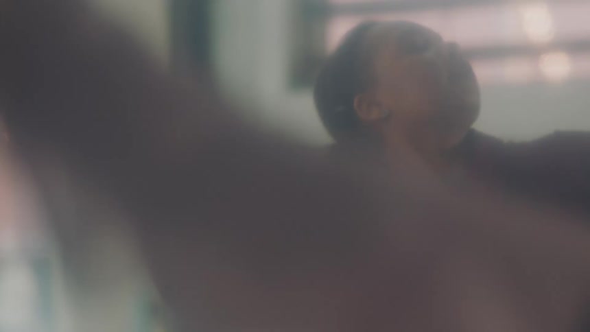 A woman in a room dancing with a plant and a wall in the background