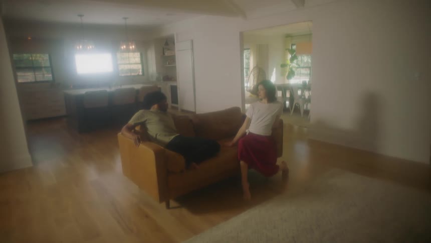 A man and a woman in a room on a couch with a wall and doorway in the background