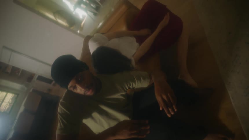 A man and a woman in a room sitting on a couch and dancing with a wall and doorway in the background